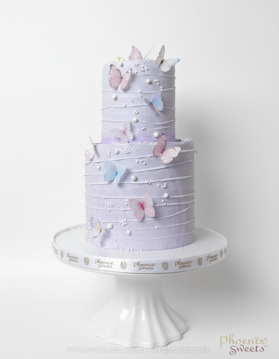 A two-tiered round cake with purple butter cream and decorated with sugar flowers and butterflies, displayed on a white cake stand.