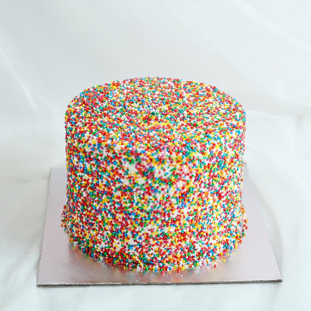 A colorful Butter Cream Cake with multicolored sprinkles on top, presented on a plate.