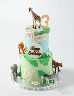 Two-tier birthday cake with animal figurines and 'Happy Birthday' text on a white background