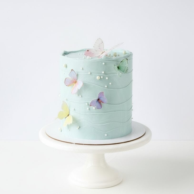 Mint green cake with butterfly decorations on a white stand against a white background